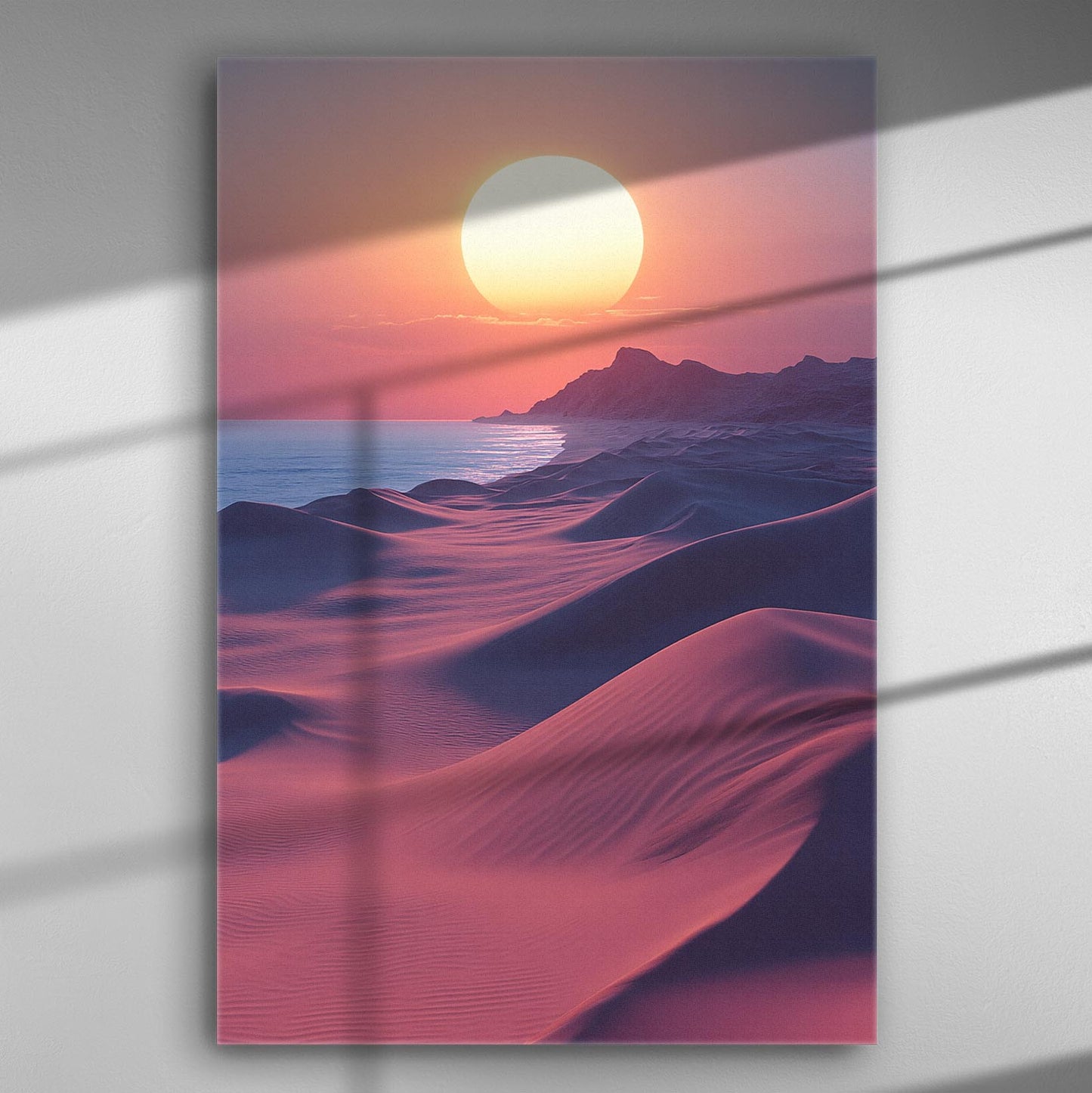 Sunset over sandy dunes with mountains in the background and a calm ocean, creating a tranquil desert landscape.