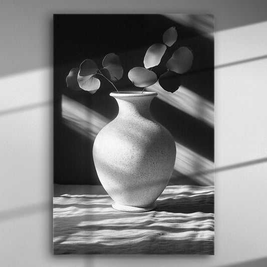 Black and white photo of a vase with leaves, where light and shadow create elegant patterns on a canvas.