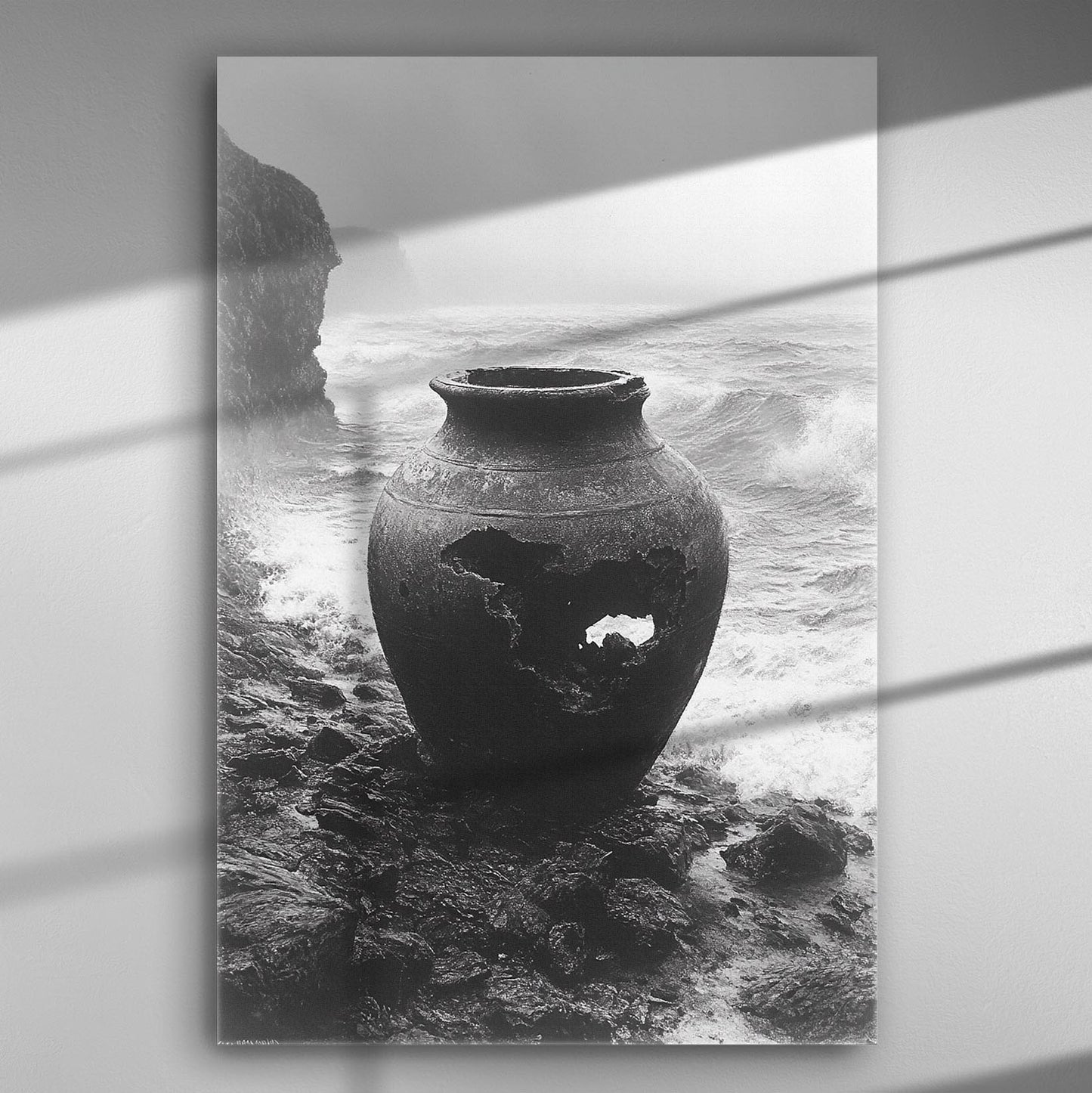 Black and white photograph of an ancient vase by the sea with waves crashing against the rocks.