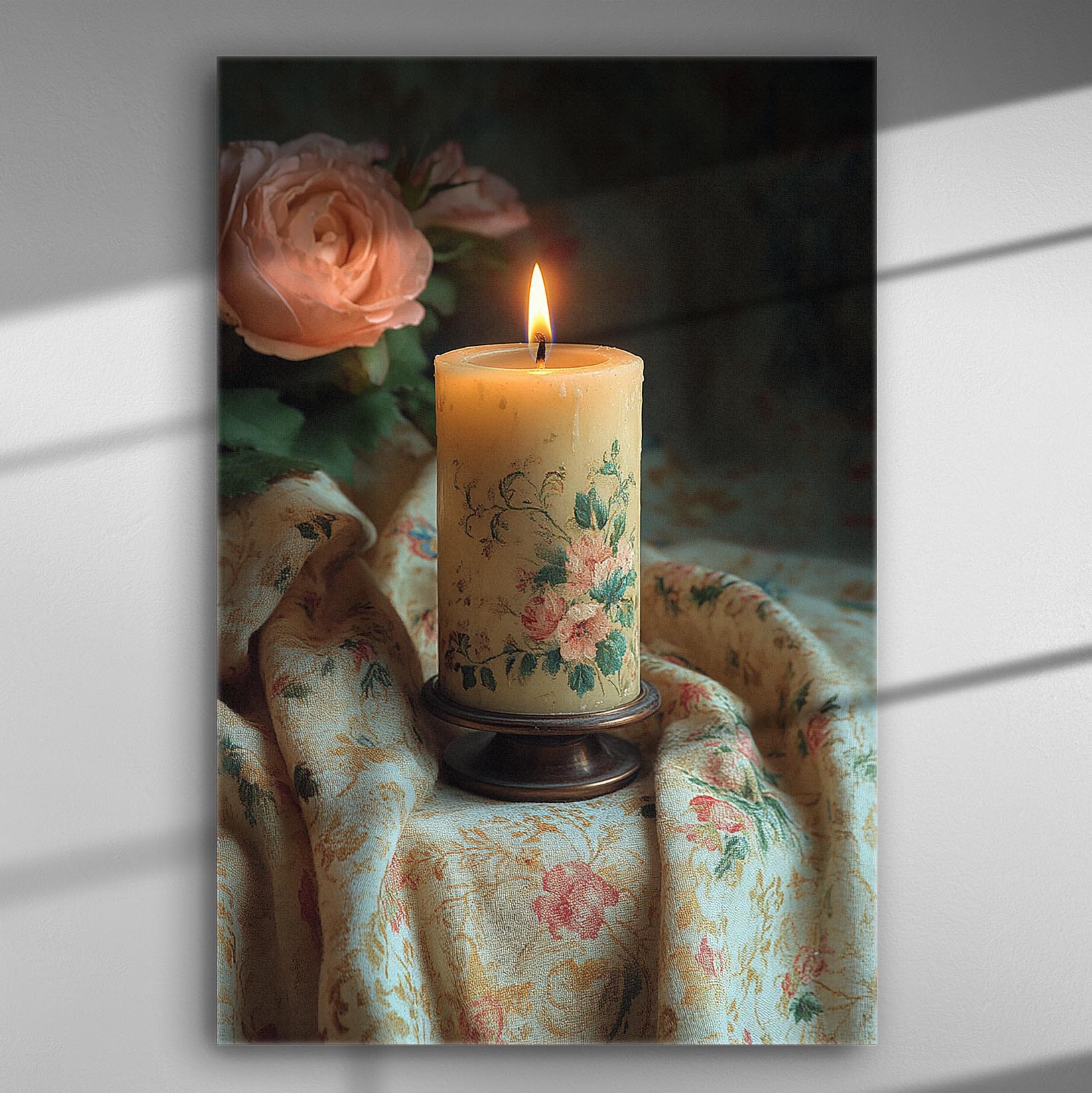 A lit candle with floral decorations beside pink roses, set on a floral-patterned fabric.