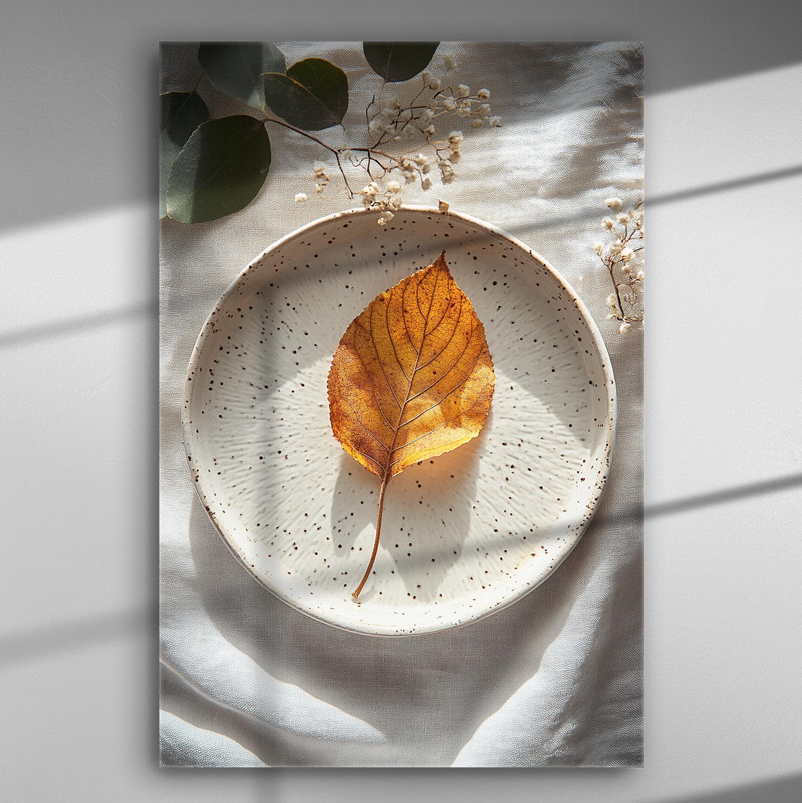 A golden autumn leaf lies on a decorative white plate with delicate lighting and shadows.