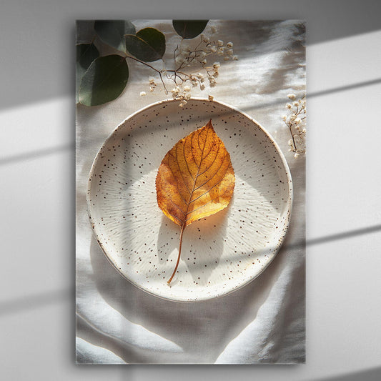 A golden autumn leaf lies on a decorative white plate with delicate lighting and shadows.