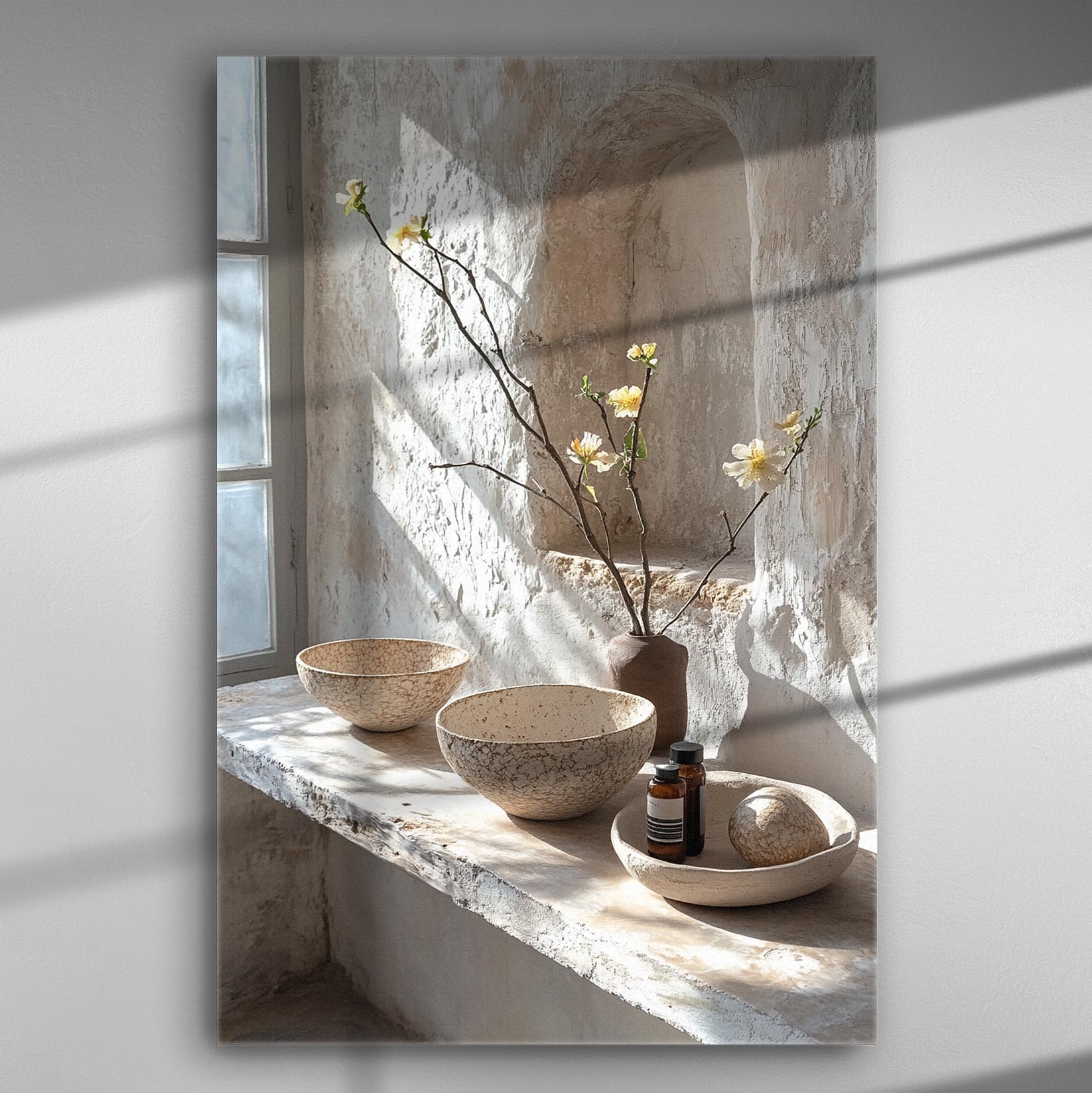 Minimalist still life with ceramic bowls, a vase with flowers, and natural light on stone shelf.